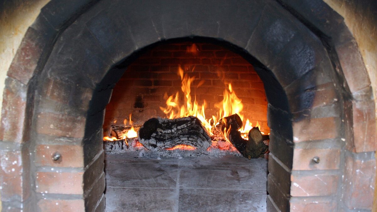 Un horno de leña de ladrillo con el fuego encendido dentro, visto de frente.