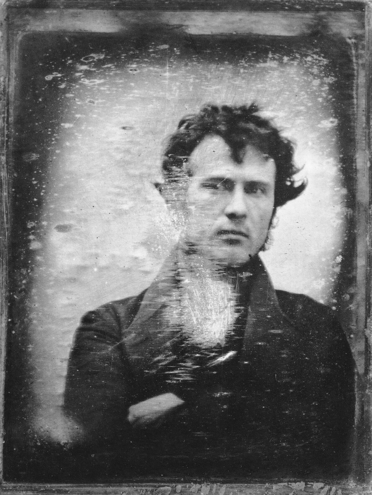 Retrato de un hombre joven de pelo revuelto y brazos cruzados, mirando ligeramente fuera de cámara.
