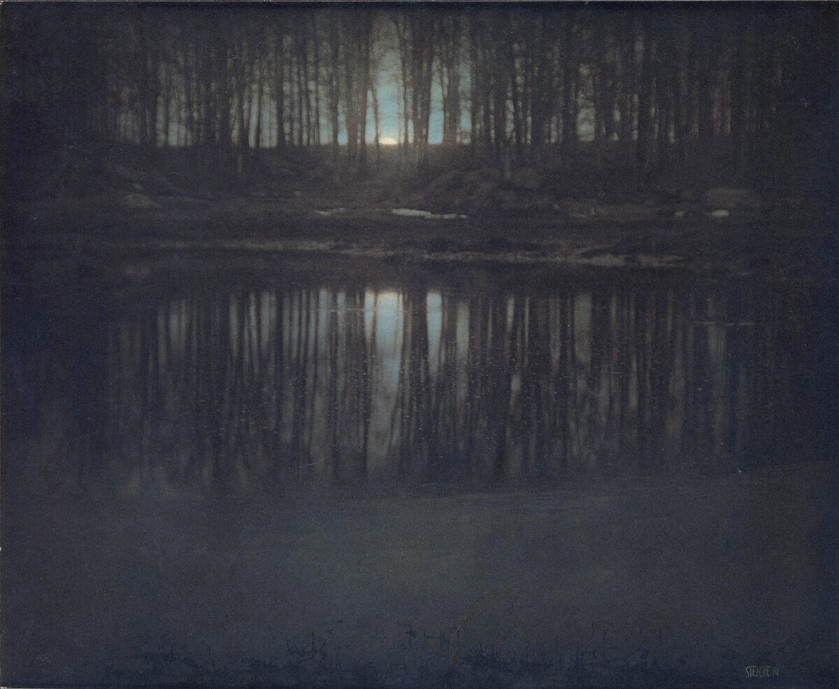 Un estanque al anochecer entre árboles, con la luna reflejada en el agua, en tonos verdes y azules.