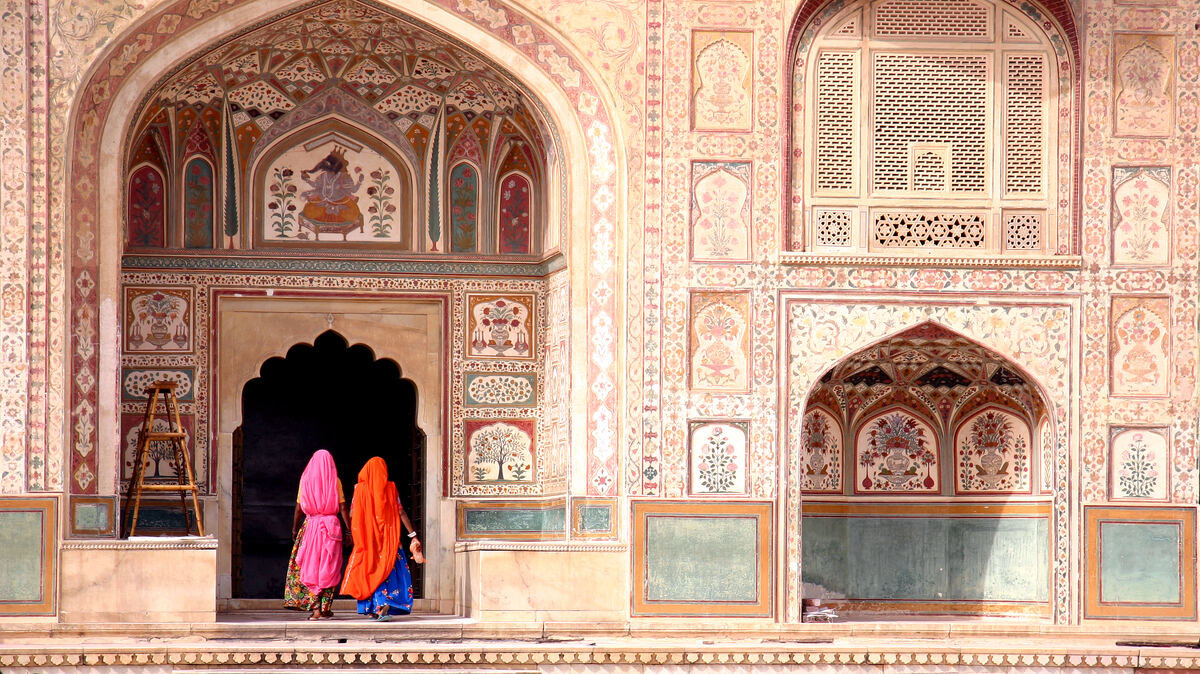 Dos mujeres con saris naranja y rosa bajo los arcos decorados del Fuerte Amber, en la India.