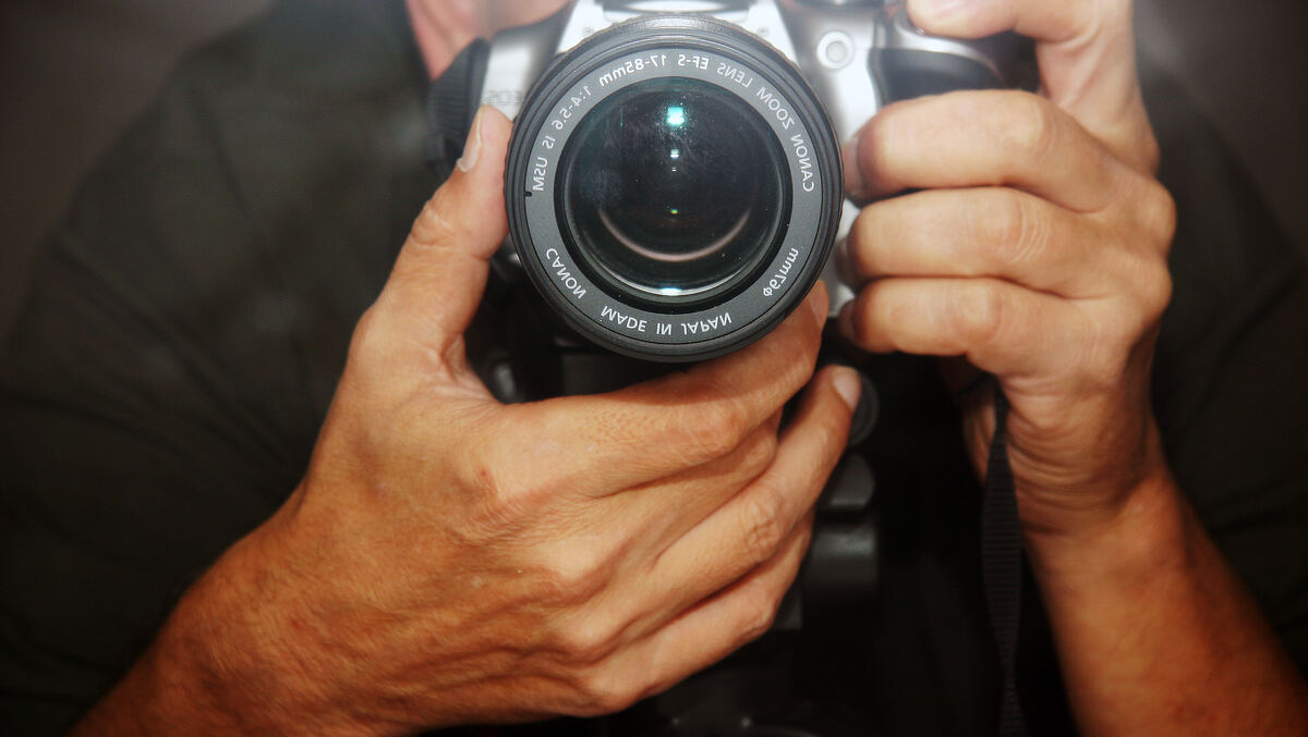 Un fotógrafo sujetando una cámara réflex con el objetivo hacia el visor.