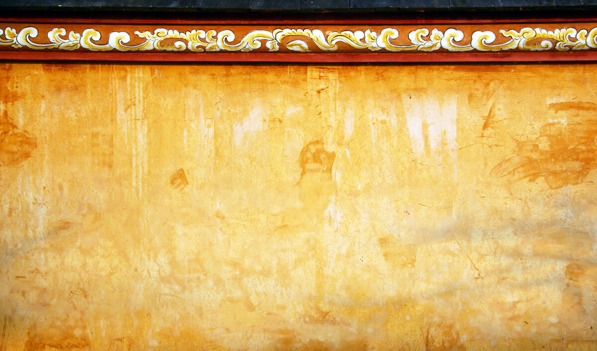 Un muro amarillo desgastado por el sol, rematado por una cenefa roja y dorada.