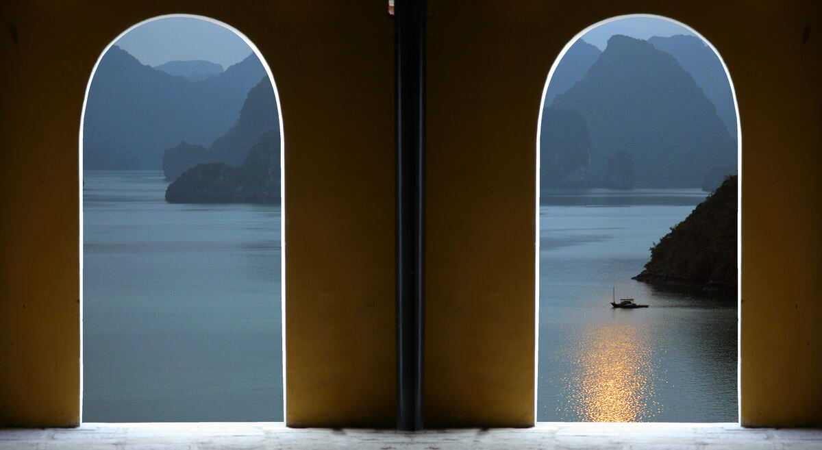 Dos ventanas en arco abiertas sobre la bahía de Halong, con el sol reflejado en el agua.